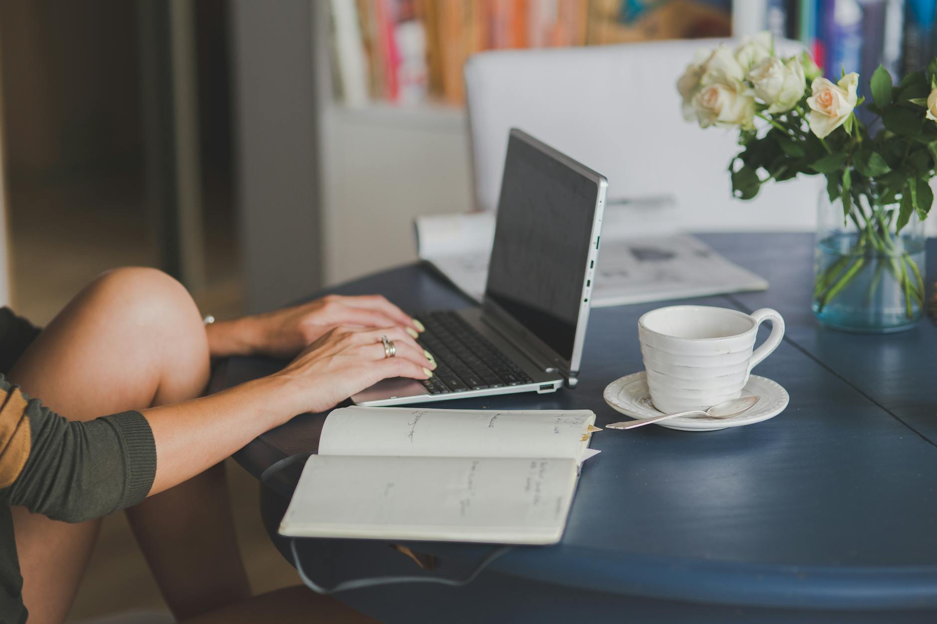 woman working with laptop at table with datebook open and  a cup of coffee on the side